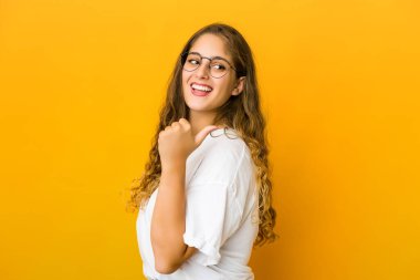 Genç beyaz kadın başparmağıyla işaret ediyor, gülüyor ve kaygısız..