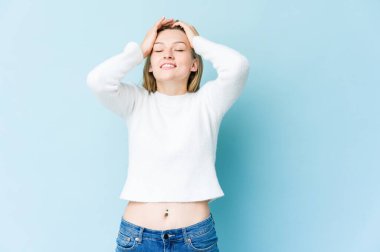 Mavi arka planda izole edilmiş genç sarışın kadın ellerini başının üstünde tutarak neşe içinde gülüyor. Mutluluk kavramı.