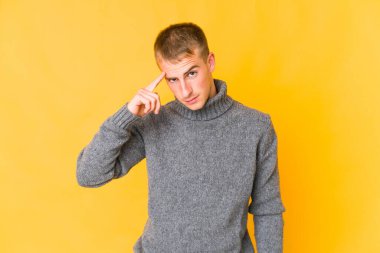 Genç, beyaz, yakışıklı bir adam şakağı parmağıyla işaret ediyor. Düşünüyor, bir göreve odaklanıyor..