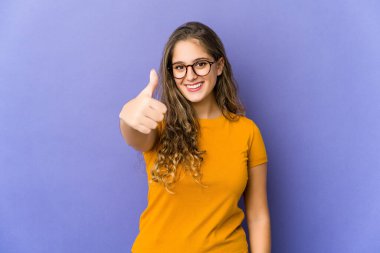 Genç, beyaz, tatlı bir kadın gülümsüyor ve başparmağını kaldırıyor.