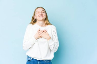 Mavi arka planda soyutlanmış genç sarışın kadın gülüyor, ellerini kalbe atıyor, mutluluk kavramını koruyor..