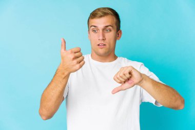 Kafkasyalı yakışıklı genç adam baş parmağını kaldırıyor ve baş parmak aşağı, zor seçim konsepti