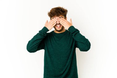 Beyaz arka plandaki genç Arap adam elleriyle gözlerini kapatıyor, gülümseyerek bir sürpriz bekliyor..