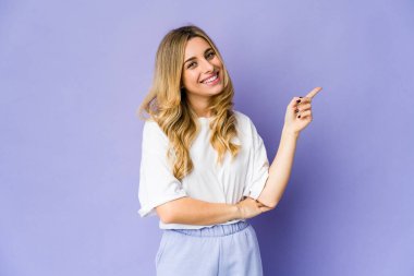 Genç, beyaz, sarışın kadın işaret parmağıyla işaret ederek gülümsüyor..