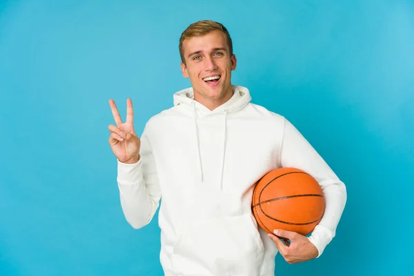 年轻的高加索人在蓝色背景下打篮球 快乐而无忧无虑 用手指展示和平的象征 — 图库照片
