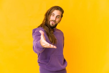 Uzun saçlı genç adam el hareketleriyle kameraya doğru uzanıyor..