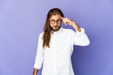 Uzun saçlı genç adam parmağıyla şakağı işaret ediyor. Düşünüyor, bir işe odaklanıyor..