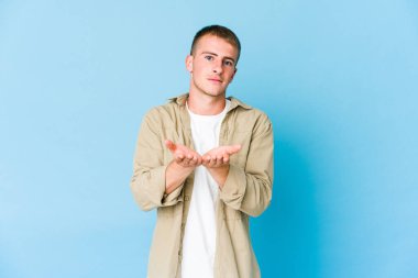 Beyaz tenli yakışıklı bir adam elinde avuç içi bir şeyle kameraya sunuyor..