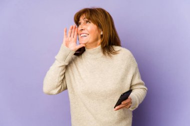 Orta yaşlı, beyaz bir kadın elinde telefonla bağırıyor ve avuç içi açık bir şekilde ağzını tutuyor..