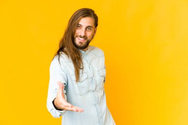 Uzun saçlı genç adam el hareketleriyle kameraya doğru uzanıyor..