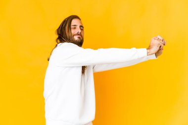 Uzun saçlı genç adam kollarını esnetiyor, rahat duruyor..