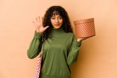 Genç Afro-Amerikan Afro kadın sevgililer günü hediyesi tutuyor. Gülümsüyor ve parmaklarıyla 5 numarayı gösteriyor..