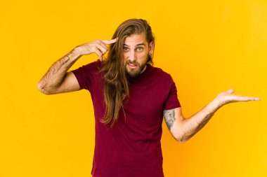 Uzun saçlı genç adam elinde bir ürünü tutuyor ve gösteriyor..