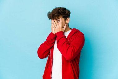 Mavi arka plandaki genç Arap parmaklarıyla gözünü kırp korkmuş ve gergin.