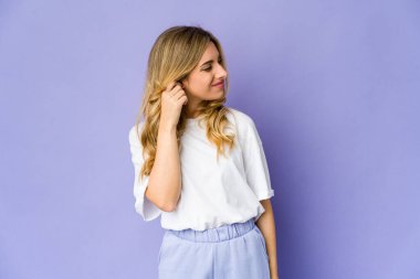 Genç, beyaz, sarışın bir kadın kulaklarını parmaklarıyla kapatıyor. Yüksek sesli bir ortam yüzünden stresli ve çaresiz..