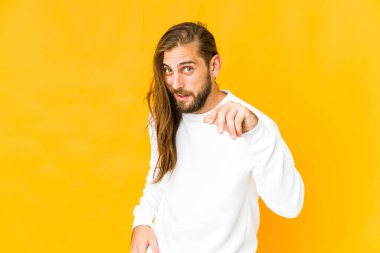 Uzun saçlı genç bir adam bir şeye gülüyor gibi görünüyor, ağzı ellerle kapatıyor..