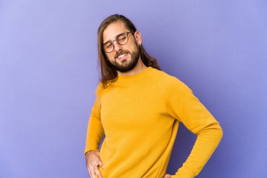 Uzun saçlı genç adam kendine güveniyor gibi görünüyor. Ellerini kalçasında tutuyor..