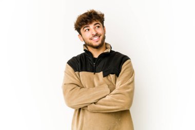 Beyaz arka plandaki genç Arap adam kollarını kavuşturarak gülümsüyor..