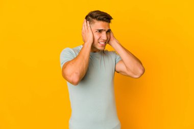 Genç, yakışıklı, beyaz bir adam izole edilmiş kulakları elleriyle kapatıyor..