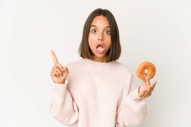 Young hispanic woman eating a doughnut having an idea, inspiration concept.