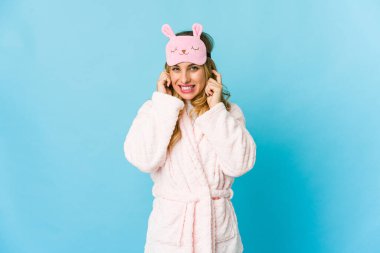 Genç sarışın, beyaz kadın pijama giyiyor kulaklarını elleriyle kapatıyor..