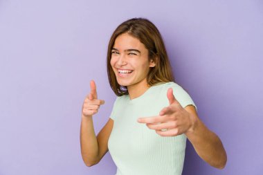 Mor arka planda genç, sıska, beyaz bir kız. Gülümsemeler öne bakıyor..