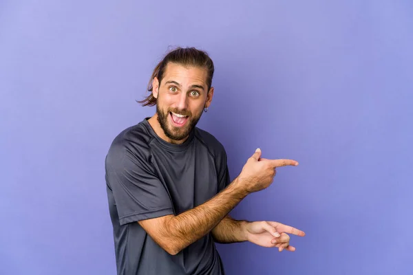 Junger Mann Mit Langen Haaren Lächelt Fröhlich Und Zeigt Mit — Stockfoto