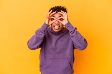 Genç Afro-Amerikalı kıvırcık adam, mor üzerine izole edilmiş, gözlerinde sorun yok işareti var.