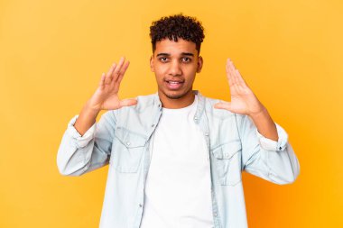 Genç Afro-Amerikan kıvırcık adamı, mor üzerine izole edilmiş, parmakları olan, gülümseyen ve kendinden emin bir şey tutuyor..