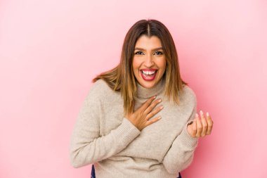 Pembe arka planda soyutlanmış genç Hintli kadın gülüyor, ellerini kalbe koyuyor, mutluluk kavramını koruyor..