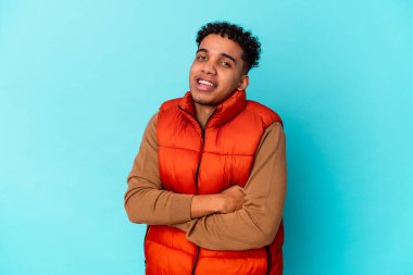 Genç Afro-Amerikan kıvırcık adamı mavi üzerine izole edilmiş, kendinden emin, kararlılıkla kollarını kavuşturuyor..