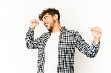 Beyaz arka planda genç bir Arap özel bir günü kutluyor, atlıyor ve enerjiyle kollarını kaldırıyor..