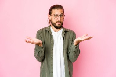 Uzun saçlı genç adam kollarıyla tartı yapıyor, mutlu ve kendinden emin..