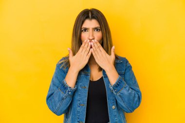 Sarı arka planda izole edilmiş genç bir Hintli kadın şok olmuş, elleriyle ağzını kapatmış, yeni bir şey keşfetmek için sabırsızlanıyor..