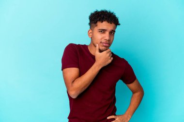 Genç Afro-Amerikalı kıvırcık adam mavi üzerine izole edilmiş, şüpheli, belirsiz, seni inceliyor..