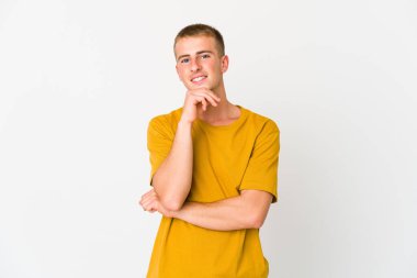 Genç beyaz yakışıklı adam gülümsüyor mutlu ve kendinden emin, çenesine elle dokunuyor..