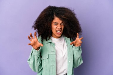 Genç Afro-Amerikalı kıvırcık kadın mor arka planda, pençelerini kedi taklidi yaparken gösteriyor, agresif bir jest..