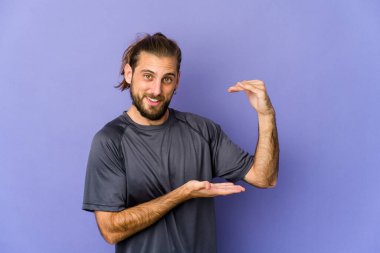 Uzun saçlı genç adam işaret parmaklarıyla küçük bir şey tutuyor, gülümsüyor ve kendinden emin..