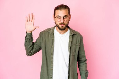 Uzun saçlı genç adam gülümsüyor. Beş numarayı parmaklarıyla gösteriyor..