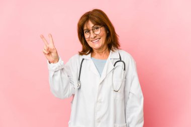 Orta yaşlı beyaz doktor kadın neşeli ve kaygısız bir şekilde parmaklarıyla barış sembolü gösteriyor..