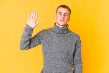 Genç beyaz yakışıklı adam gülümseyerek beş numarayı parmaklarıyla gösteriyor..