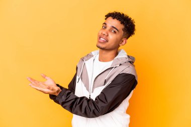 Genç Afro-Amerikalı kıvırcık adam, mor üzerine izole edilmiş. Elinde palmiye ağacında bir kopya alanı var..