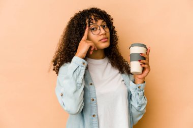 Afro-Amerikalı genç bir kadın elinde hazır kahveyle tapınağı işaret ediyor, düşünüyor ve bir göreve odaklanıyor..