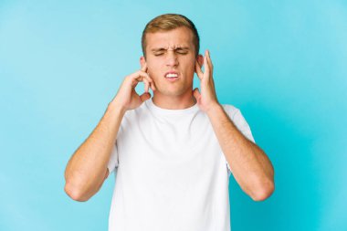 Genç, beyaz, yakışıklı bir adam kulaklarını parmaklarıyla kapatıyor. Yüksek sesli bir ortam yüzünden stresli ve çaresiz..