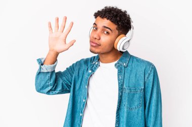 Genç Afro-Amerikalı kıvırcık adam kulaklıkla müzik dinleyip beş numarayı parmaklarıyla gülümsüyor..