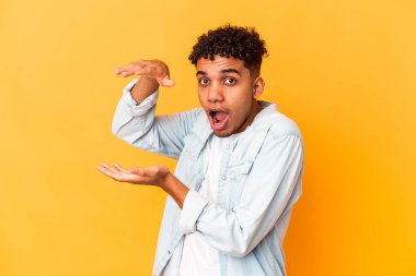 Genç Afro-Amerikan kıvırcık adamı, mor renkte izole edilmiş, şok olmuş ve hayret içinde, elleri arasında bir kopya alanı tutuyor..