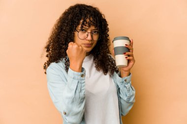 Afro-Amerikan Afro kadın elinde hazır kahveyle kameraya yumruk sallıyor, agresif yüz ifadesi var..