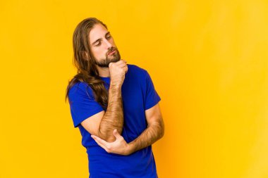 Uzun saçlı genç adam şüpheli ve kuşkulu bir ifadeyle yana bakıyor..