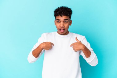Genç Afro-Amerikan kıvırcık adamı mavi üzerine izole edilmiş, parmağını göstererek şaşırmış, geniş bir gülümsemeyle.