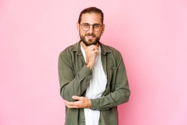 Uzun saçlı genç adam gülümsüyor mutlu ve kendinden emin, çenesine elle dokunuyor..